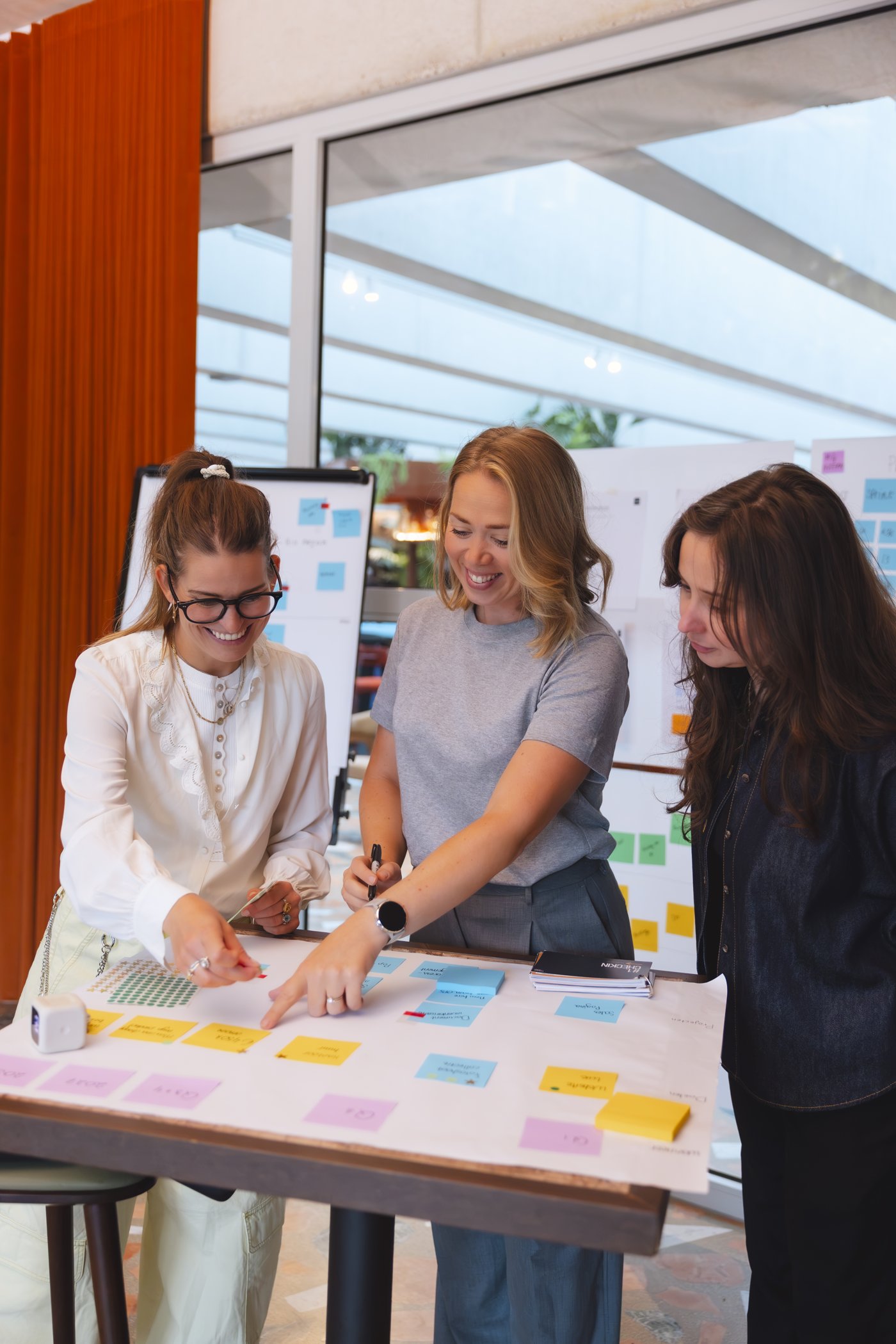 Elke wijst iets aan op een tafel vol post-its, samen met twee ondernemers
