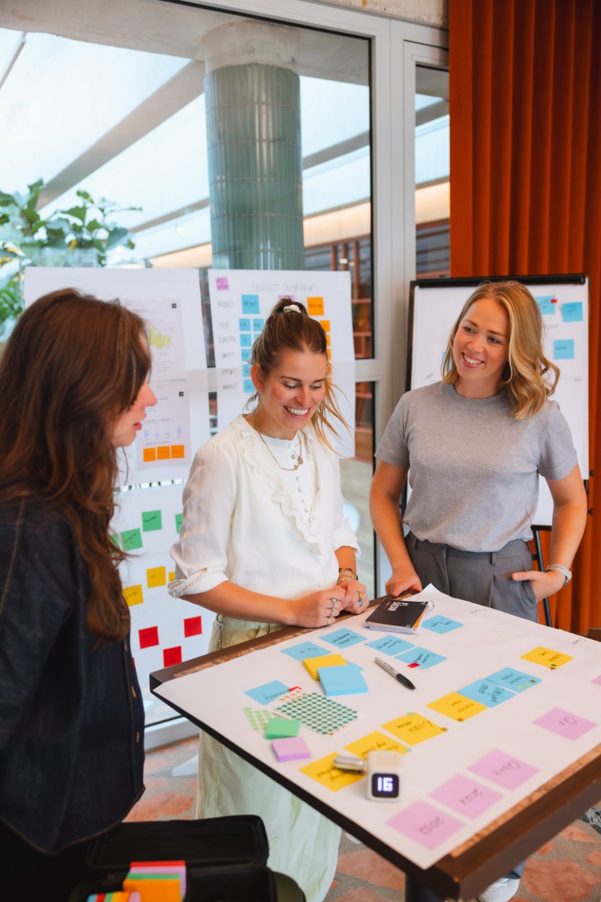 Drie vrouwen lachend aan een tafel met post-its